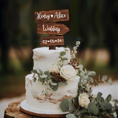 a white wedding cake with greenery and wooden sign