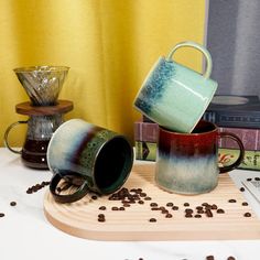 three coffee mugs sitting on top of a wooden tray with coffee beans scattered around them