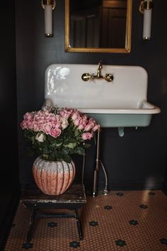 a white sink sitting under a mirror next to a vase with pink flowers in it