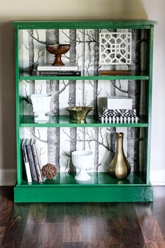 a green bookcase with books and vases on it in front of a wall