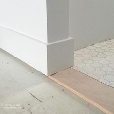 the corner of a white building with a tile floor next to it and an unfinished piece of wood on the ground