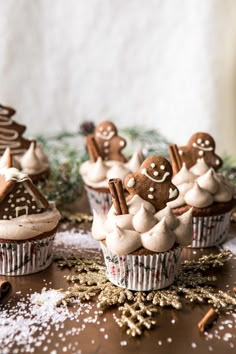 some cupcakes with frosting and gingerbread decorations on them are sitting on a table