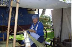 an old man is working on some kind of spinning wheel in front of a blue wagon