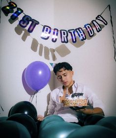 a man sitting in front of a birthday cake with balloons and streamers around him