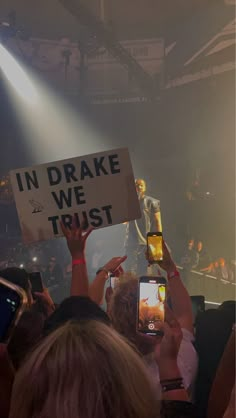 people holding up cell phones in front of a stage with lights and signs reading in drake we trust