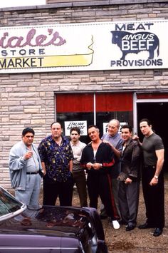 a group of men standing in front of a butcher's shop posing for a photo