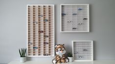 a stuffed tiger sitting on top of a white desk next to two framed pictures and a potted plant