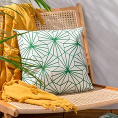 a green and white pillow sitting on top of a wooden chair next to a plant