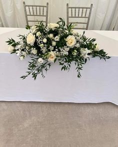 white flowers and greenery are arranged on top of the head table at this wedding reception