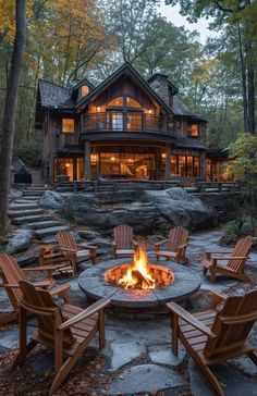 a fire pit with chairs around it in front of a large house surrounded by trees