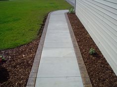 a sidewalk next to a white house and green grass