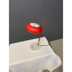 a red and white lamp sitting on top of a table next to a white table cloth