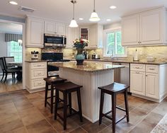 a large kitchen with white cabinets and marble counter tops, two stools at the island