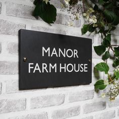 a sign that reads manor farm house hanging on a brick wall next to some flowers