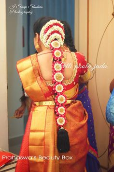 the back of a woman's head wearing an orange and red saree with flowers on it