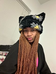 a young man with long braids wearing a knitted cat hat and black jacket