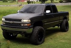 a large black truck parked on top of a lush green field