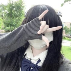 a woman with long black hair wearing a gray sweater and holding her hands up to her face