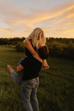 two people standing in the grass with their arms around each other as the sun sets