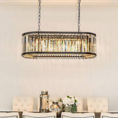 a chandelier hanging over a dining room table with white upholstered chairs