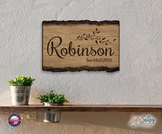 a wooden sign hanging on the side of a wall next to two potted plants