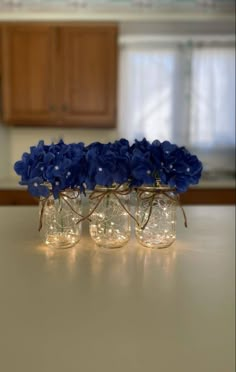 three mason jars filled with blue flowers sitting on top of a counter