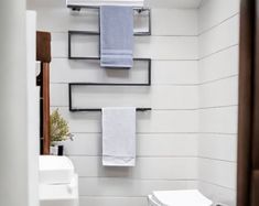 a white toilet sitting next to a bathroom sink under a towel rack with two towels hanging on it