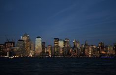 the city skyline is lit up at night as seen from across the water in new york