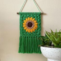 a crocheted wall hanging with a sunflower on it and a potted plant