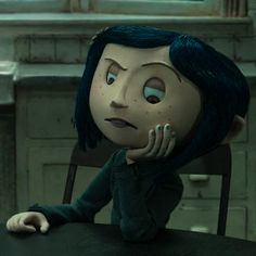 an animated doll sitting at a table with her hand on her chin and looking to the side