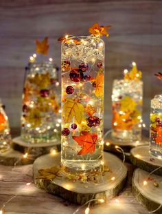 lighted glass vases with autumn leaves and berries on them are sitting on wood slices