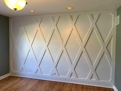 an empty room with wood flooring and white wallpaper on the walls, in front of a light fixture