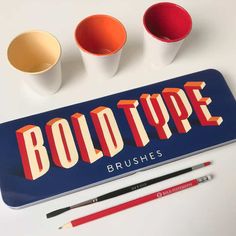 three cups and two pencils sitting on top of a blue sign that says bold type brushes