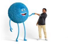 a man standing next to a giant blue ball with arms and legs, pointing at it