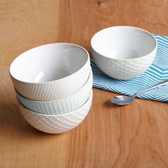 three white bowls on a wooden table with spoons next to them and a blue napkin