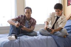 two boys sitting on a bed playing video games