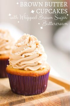 two cupcakes with whipped cream frosting sitting on a cutting board next to each other