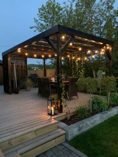 a gazebo with string lights on it in the middle of a garden area at dusk