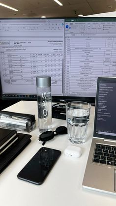 a laptop computer sitting on top of a desk next to a glass of water and cell phone