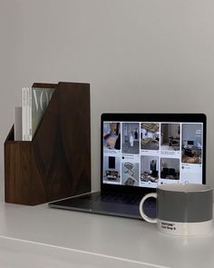 an open laptop computer sitting on top of a desk next to a cup and book