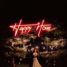 a bride and groom standing in front of a neon happy hour sign at their wedding