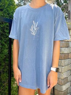 "Comfort Colors blue t-shirt with a flower in white. T-Shirt Color: Comfort Colors \"blue jean\" ✰ MODEL INFO: ✰ Height: 5'4\" Size: modeling a large. (Normally wears a small). *SIZE UP FOR AN OVERSIZED LOOK* ★ MATERIAL: ★ 100% cotton Unisex/Adult sizing." Trendy Light Blue Spring T-shirt, White Denim Short Sleeve Top, White Short Sleeve Denim Tops, Trendy Blue Denim T-shirt, Casual Blue Denim T-shirt, Denim Blue Crew Neck Top For Spring, Light Blue Cotton T-shirt For Spring, Denim Short Sleeve T-shirt For Spring, Trendy Blue T-shirt For Spring