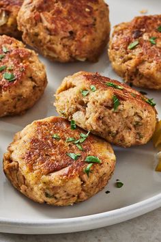 several crab cakes on a white plate with lemon wedges and parsley sprig