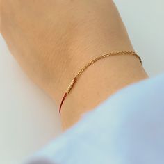 Close-up of hand wearing delicate bracelet of gold chain and red thread with gold beads detail at center. Elegant Friendship Bracelets With Adjustable Chain, Dainty Gold Friendship Bracelets For Everyday, Minimalist Gold Friendship Bracelets For Everyday, Minimalist Gold Friendship Bracelet For Everyday, Minimalist Everyday Friendship Bracelets, Minimalist Adjustable Gold Bracelet With Chain, Minimalist Adjustable Gold Chain Bracelet, Elegant Yellow Gold Friendship Bracelets As Gift, Everyday Elegant Rose Gold Friendship Bracelets