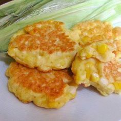 three corn cakes on a plate next to an ear of corn