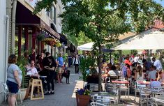 many people are sitting at tables outside on the sidewalk in front of shops and restaurants