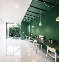 an empty room with green walls and white chairs in the center is lit by hanging lights