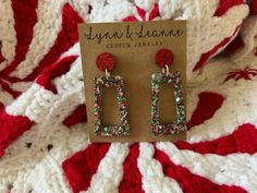 a pair of earrings with red and green beads sitting on top of a knitted blanket