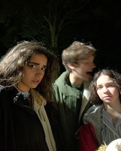 three young people standing next to each other in front of a tree at night time