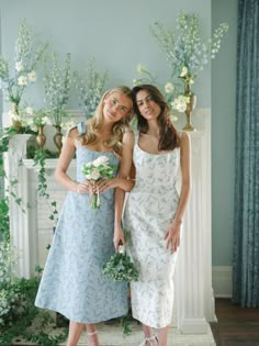 two beautiful young women standing next to each other in front of a fireplace with flowers